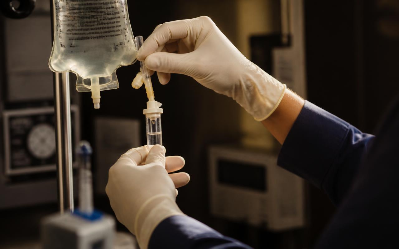 A clinician's gloved hands preparing an intravenous infusion line in a treatment room.