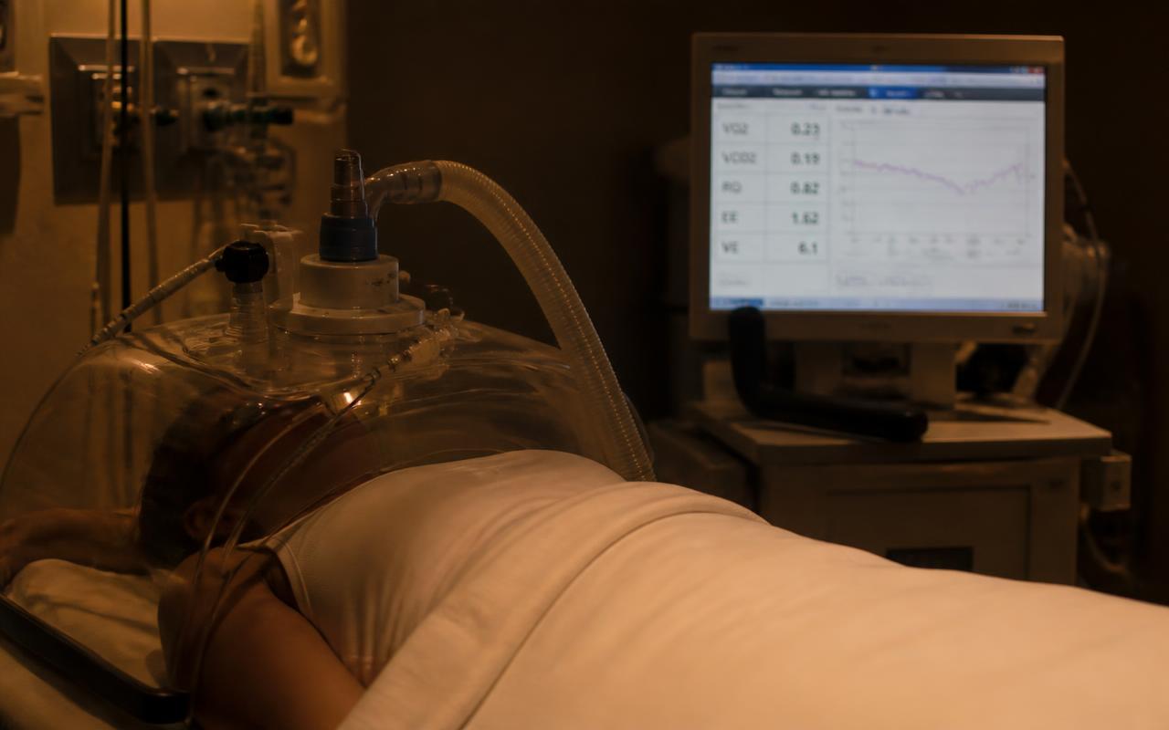 A metabolic measurement canopy positioned over a person lying still on a clinic bed.